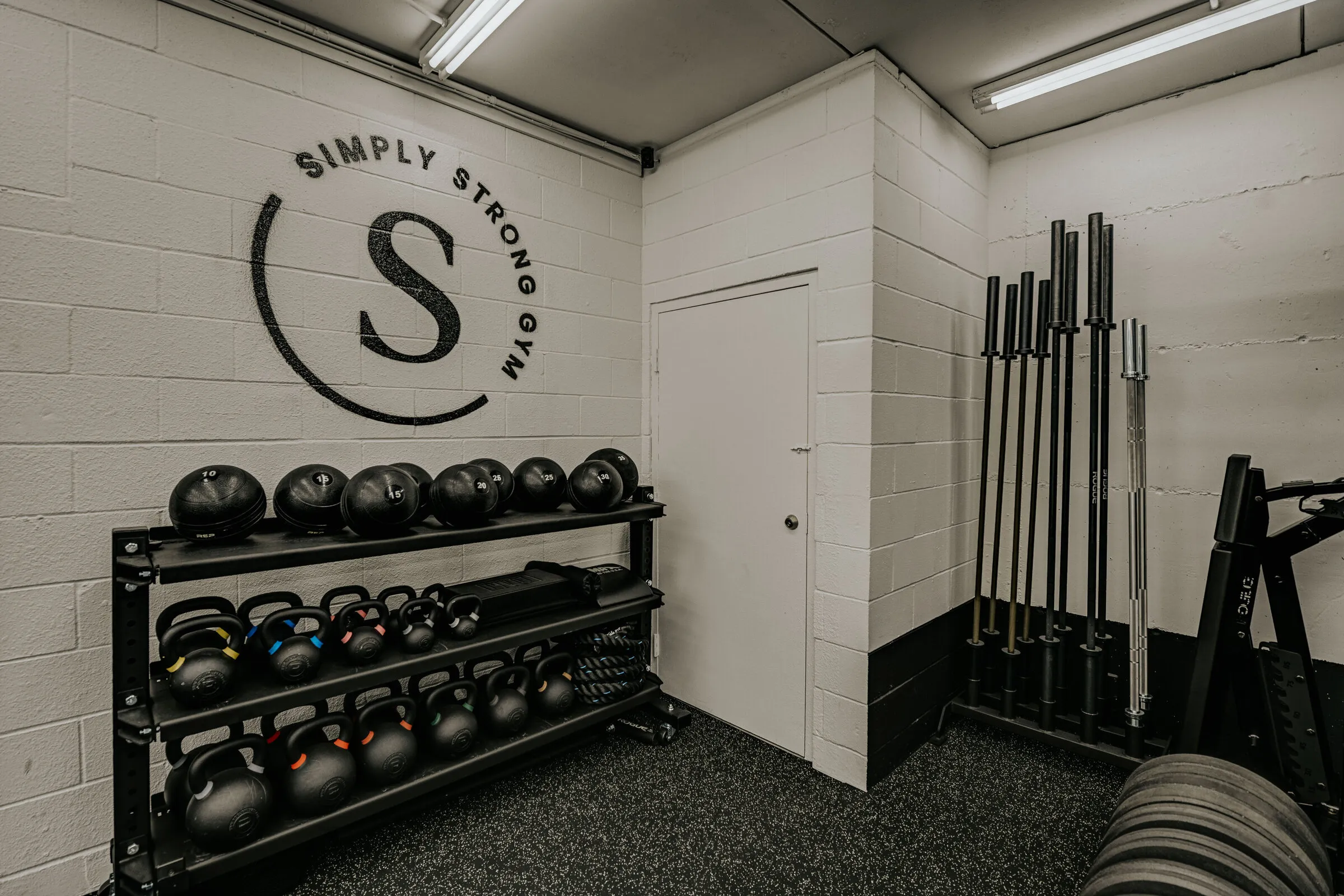 Medicine balls, kettlebells and barbells beneath the Simply Strong Gym logo