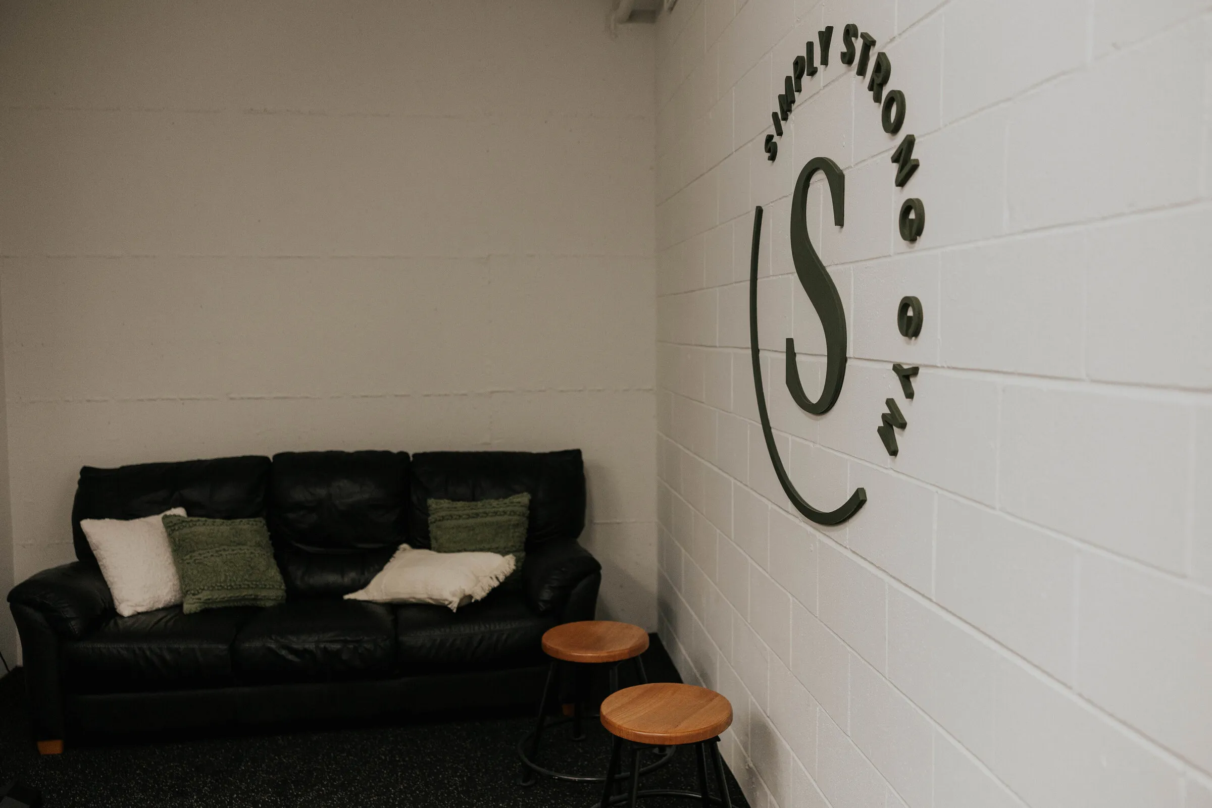 The lounge corner — a couch and stools beside the Simply Strong Gym logo wall